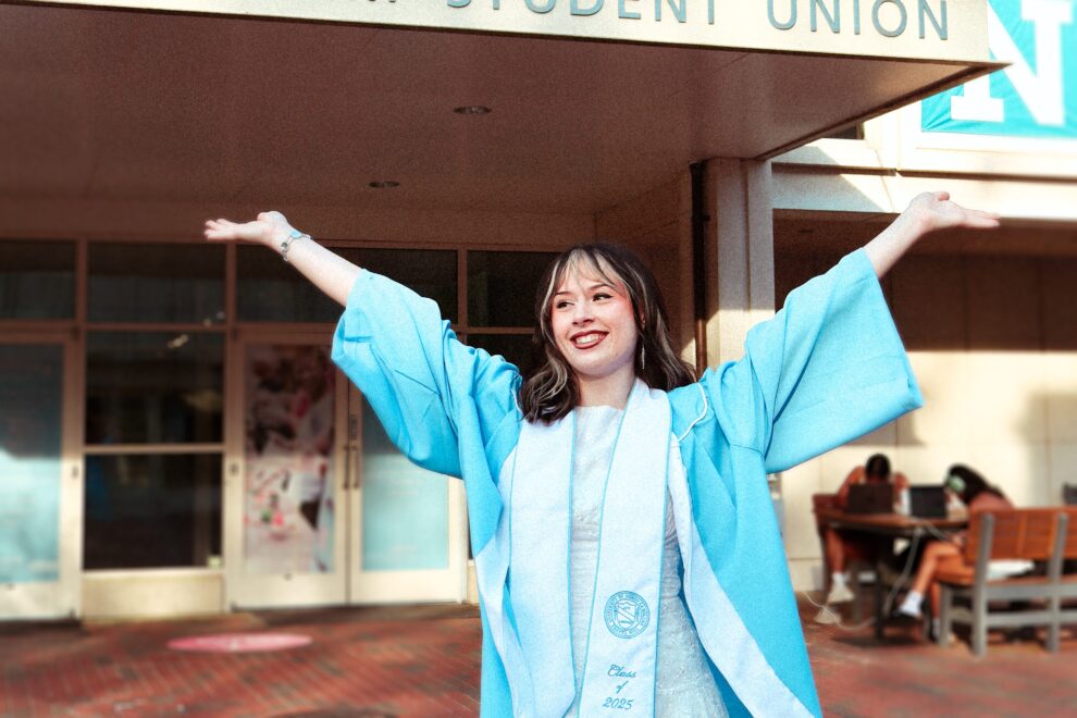 Student staff member Savannah Nelson poses in from of the Union in graduation attire for grad photos.