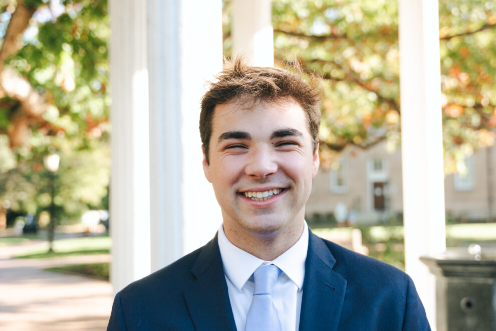 A person stands in front of the Old Well while wearing a suit
