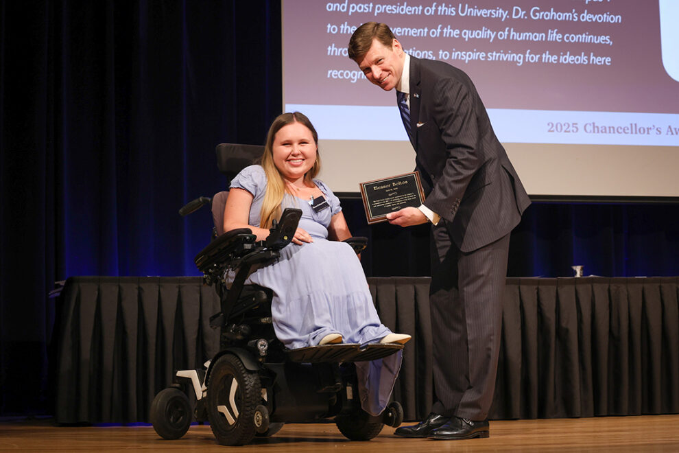Photo of UNC Chancellor Lee Roberts on stage giving an award to a UNC student during the 2025 Chancellor Awards. The award ceremony took place in the Great Hall of the Carolina Union. Photo Credit: HuthPhoto | Erin Scannell