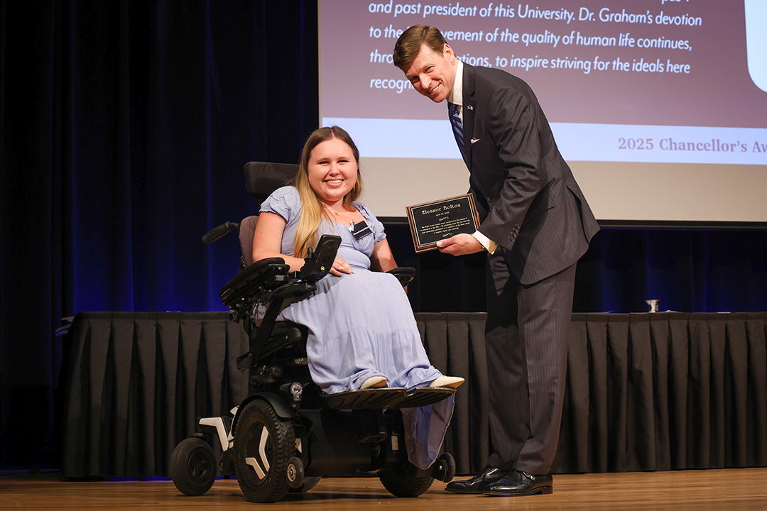 Photo of UNC Chancellor Lee Roberts on stage giving an award to a UNC student during the 2025 Chancellor Awards. The award ceremony took place in the Great Hall of the Carolina Union. Photo Credit: HuthPhoto | Erin Scannell