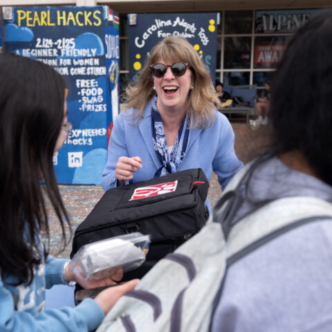 A woman wearing a suit and sunglasses passes out lunch in the Pit on a college campus