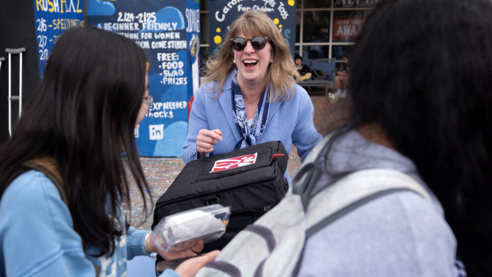 A woman wearing a suit and sunglasses passes out lunch in the Pit on a college campus