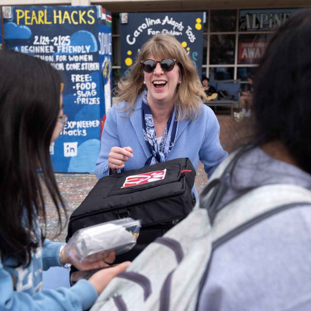 A woman wearing a suit and sunglasses passes out lunch in the Pit on a college campus