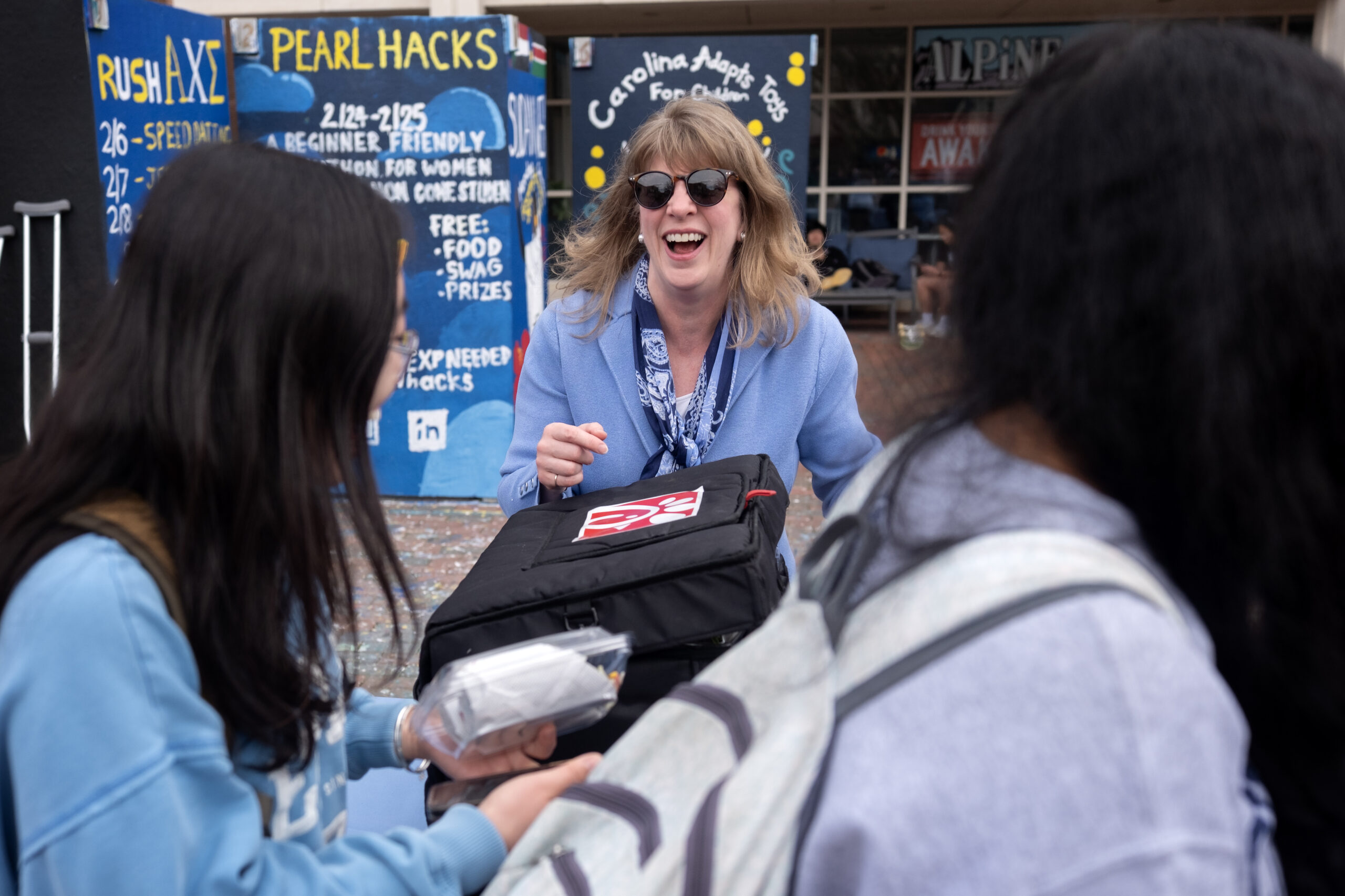 A woman wearing a suit and sunglasses passes out lunch in the Pit on a college campus