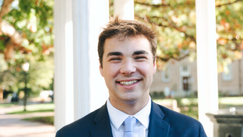 A person stands in front of the Old Well while wearing a suit.