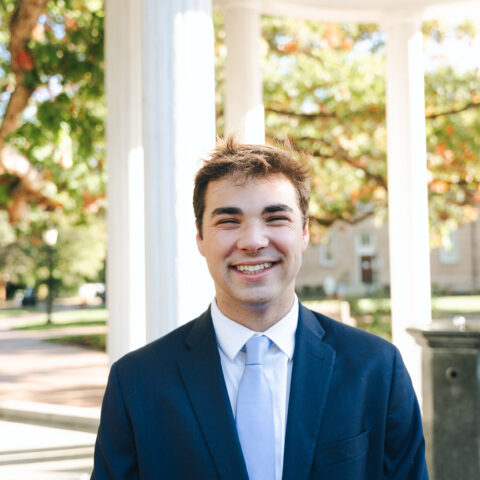 A person stands in front of the Old Well while wearing a suit.