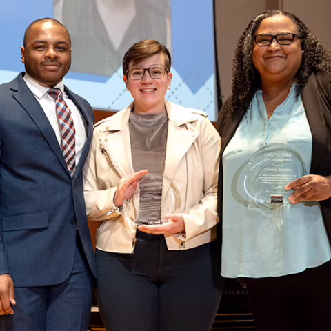Three people standing pose for an award photo